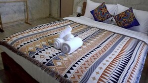 Ein Bett mit einem gemusterten Überwurf, Kissen und zusammengerollten Handtüchern.