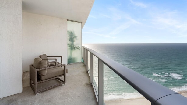 Un balcon avec un canapé en osier et une porte vitrée, donnant sur une plage et l’océan.
