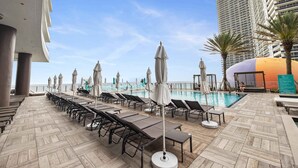 Un espace aménagé au bord de la piscine, avec des chaises longues, des parasols et une vue sur l’océan.