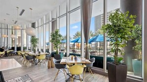 Un espace de restauration moderne, doté de grandes fenêtres, de plantes d’intérieur et de chaises jaunes.