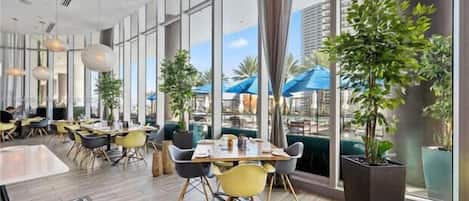 A modern dining area with large windows, indoor plants, and yellow chairs.