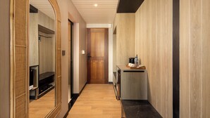 A hallway with a wooden floor, a mirror, a wooden door, and a small table with a coffee maker. - Amankara Canggu (Tibubeneng)