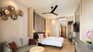 A modern hotel room with a bed, a sofa, a small round table, a ceiling fan, and a TV. - Amankara Canggu (Tibubeneng)