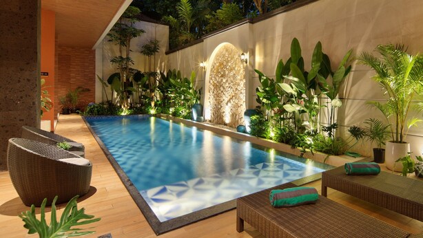 A modern outdoor pool area with lounge chairs, a stone wall, and lush greenery. - Amankara Canggu (Tibubeneng)