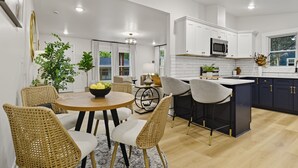 Una cocina moderna con armarios blancos, una isla central y una zona de comedor con sillas de mimbre.