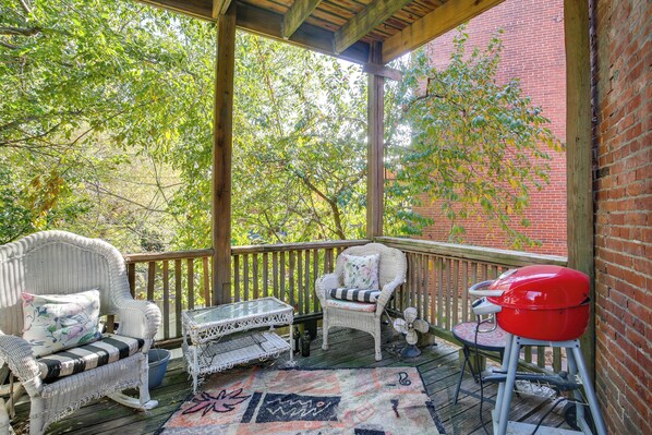 A covered porch with wicker furniture, a red grill, and a view of trees and a brick wall. - Heart of St Louis! Walkable Soulard Apt w/ Loft (St. Louis)