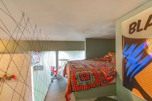 A room with a colorful quilted bedspread, a hanging net, and a poster on the wall. - Heart of St Louis! Walkable Soulard Apt w/ Loft (St. Louis)