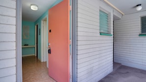 Un couloir avec une porte fermée, une petite fenêtre avec des volets et un luminaire au plafond.