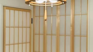 Ein Zimmer mit einer raumteilenden Shoji-Schiebetür, einer hängenden Leuchte und einer Holzbalkendecke.