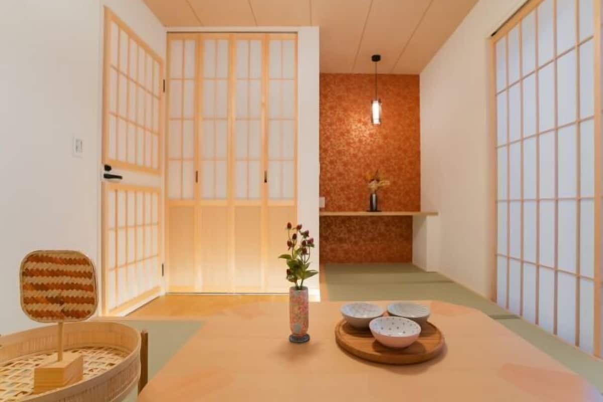 Een traditionele Japanse kamer met tatami vloeren, glijdende deuren, een tafel met kommen en een vaas met bloemen.