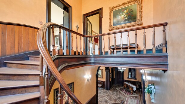 A grand staircase with wooden balusters and a handrail, leading to a landing with a patterned floor and a mirror. - Walk to Golf Course: Spacious Rough River Retreat! (Falls of Rough)