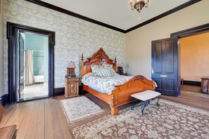 Ein Schlafzimmer mit einem hölzernen Bett, einer Sitzbank, einem Nachttisch und einer Tür.