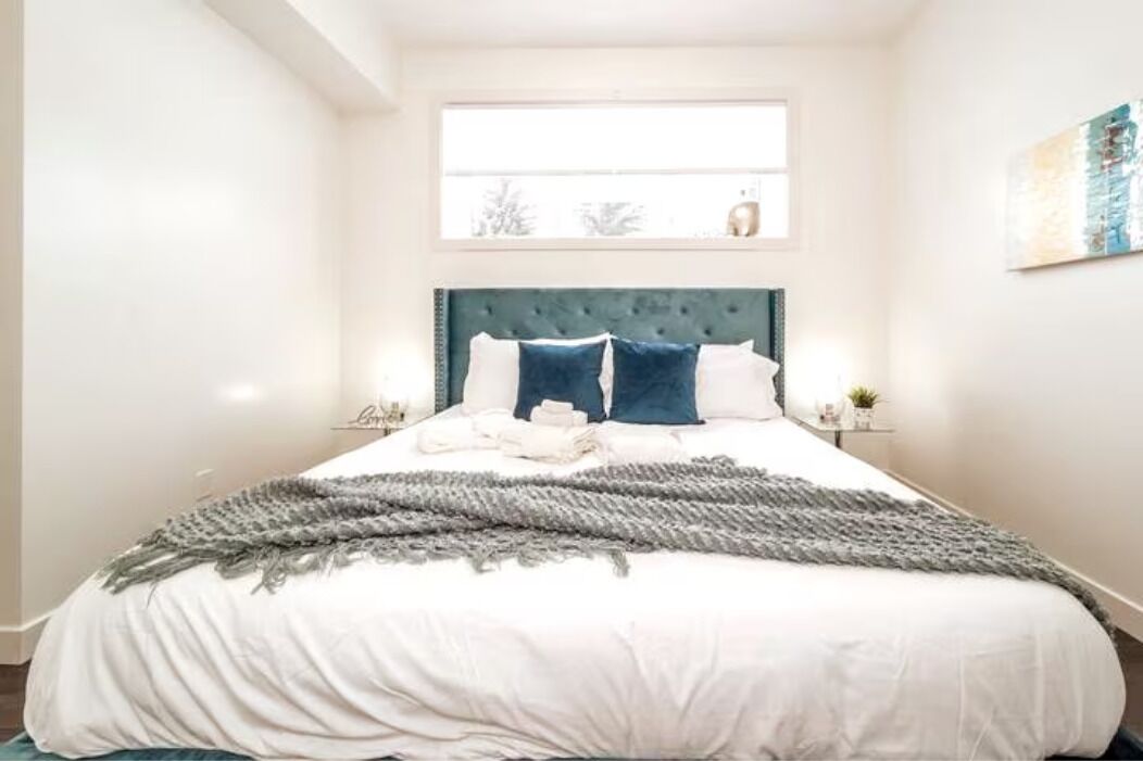 A neatly made bed with a grey throw blanket, white bedding, and two blue pillows.