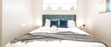 A neatly made bed with a grey throw blanket, white bedding, and two blue pillows.