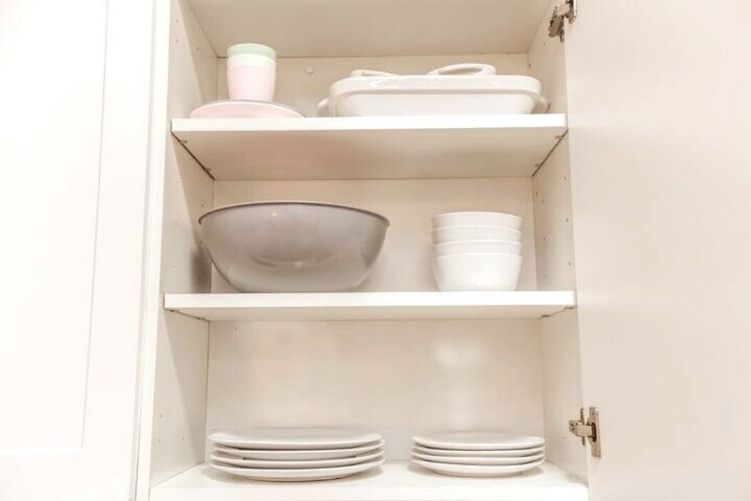 A white cabinet with three shelves, each containing white bowls and plates.