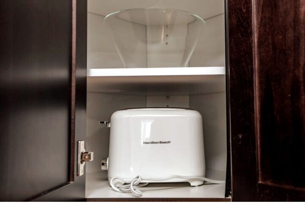 A white Hamilton Beach toaster in a wooden cabinet with a glass door.