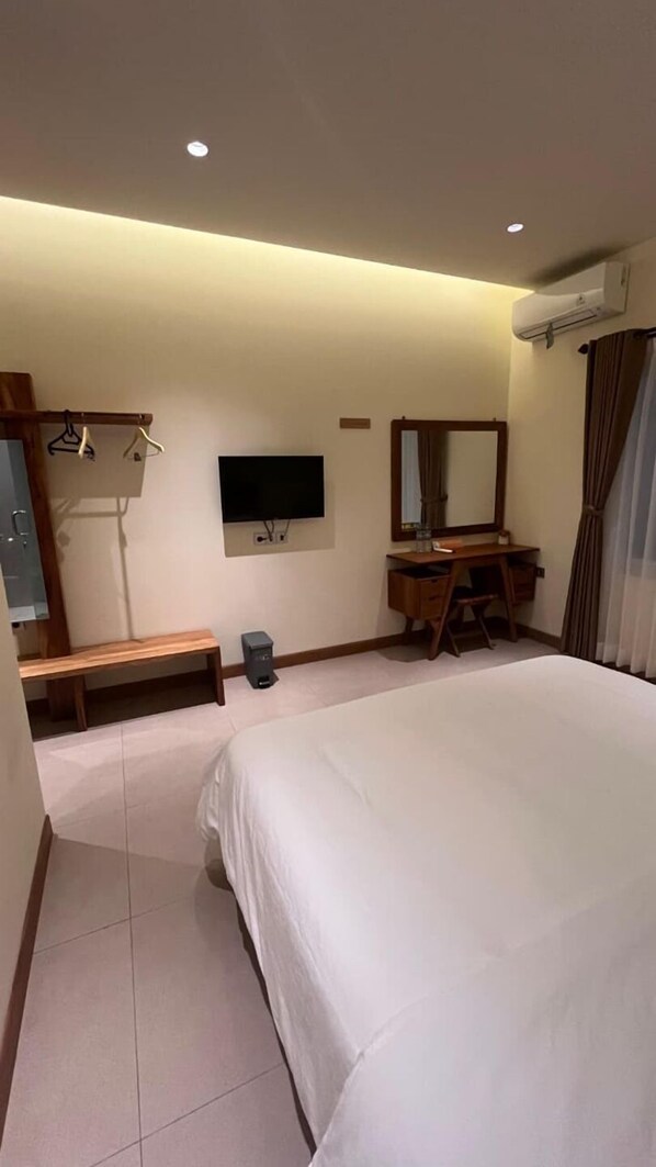 A hotel room with a large bed, a desk with a chair, a TV mounted on the wall, a mirror, and a coat rack with hangers.