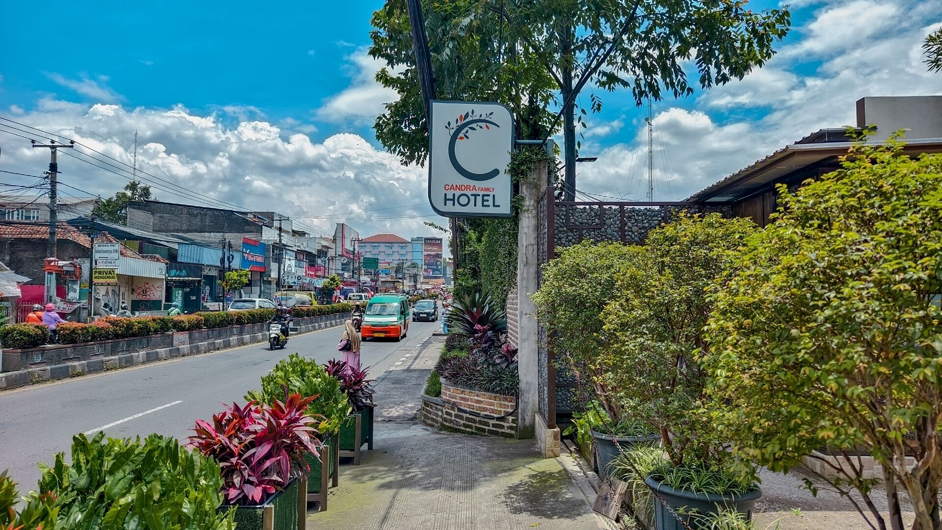 Entrada de hotel com placa, vista da rua com veículos e vegetação.