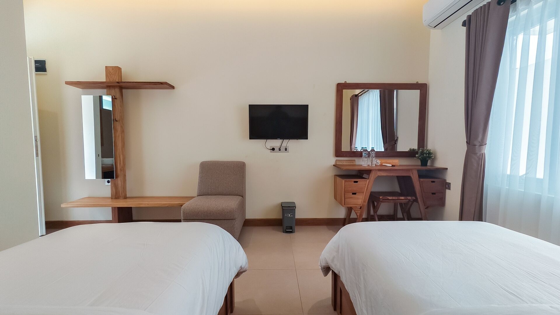 Une chambre d’hôtel avec deux lits, un bureau, une chaise, une télévision, un miroir et une étagère en forme de croix.