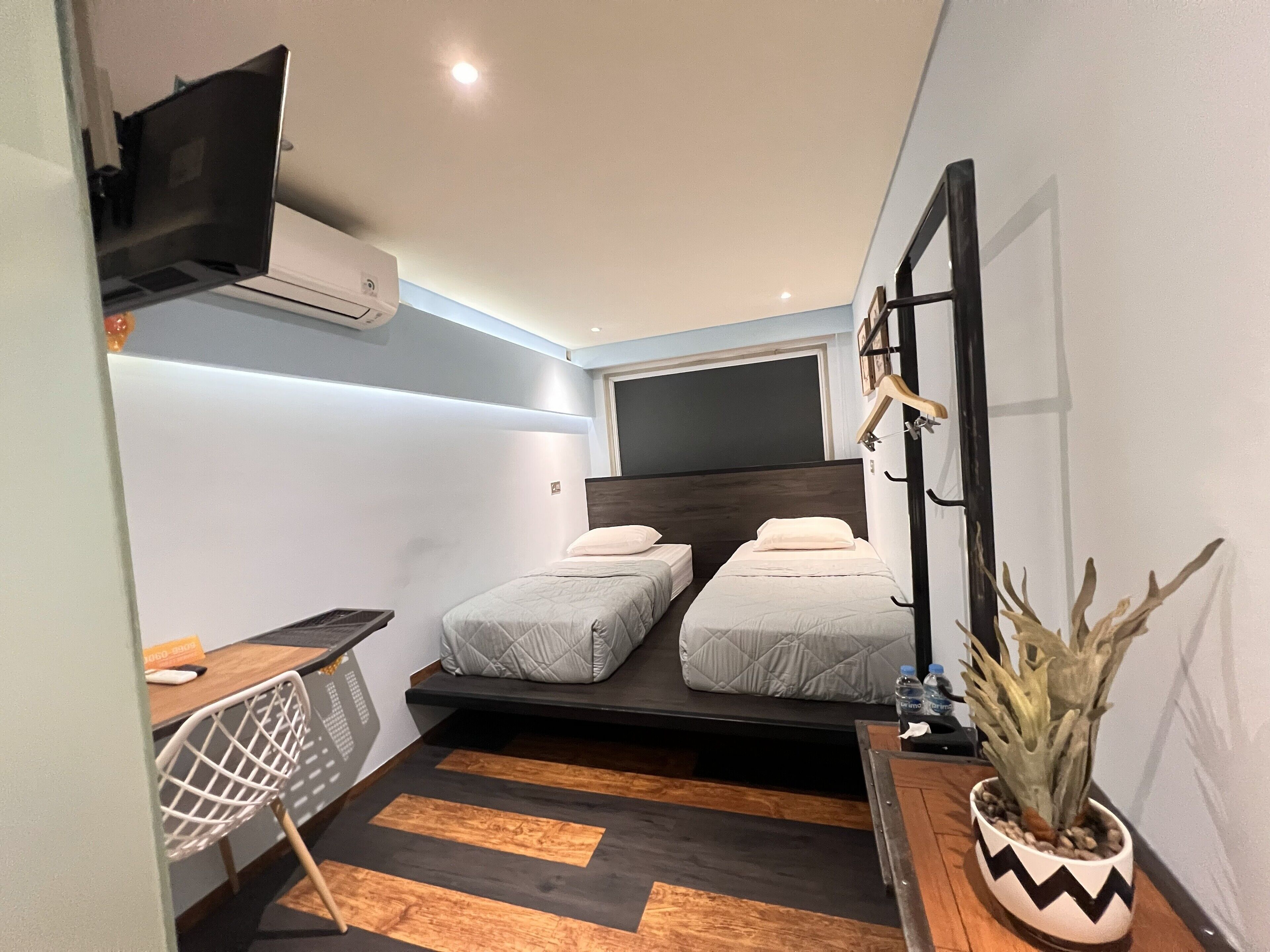 Habitación de hotel pequeña con dos camas, un escritorio, una silla, un televisor y una planta en maceta.