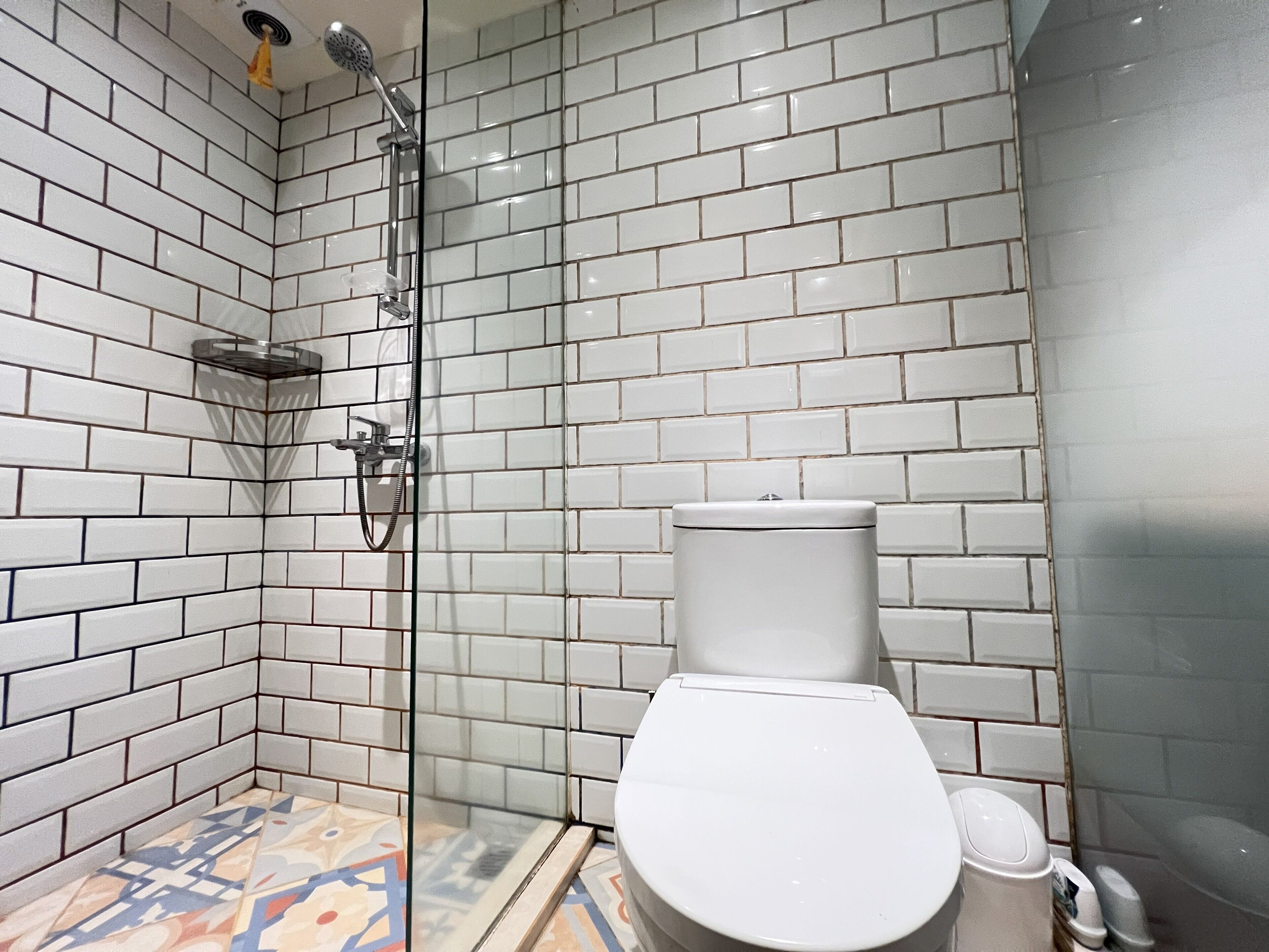 A bathroom with white subway tiles, a glass shower enclosure, and a toilet.