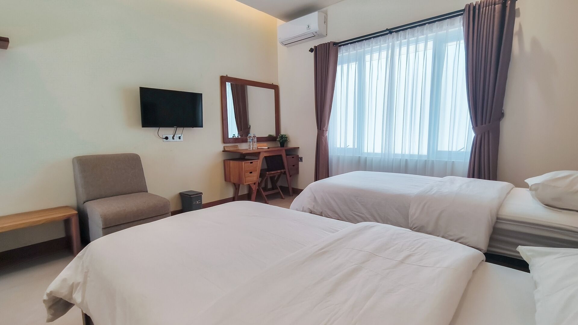 A hotel room with two beds, a desk with a chair, a TV, and a window with curtains.