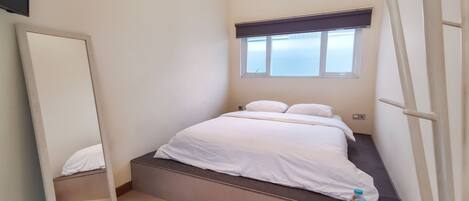 Un dormitorio pequeño y ordenado, con cama, ventana, espejo y una botella de agua.