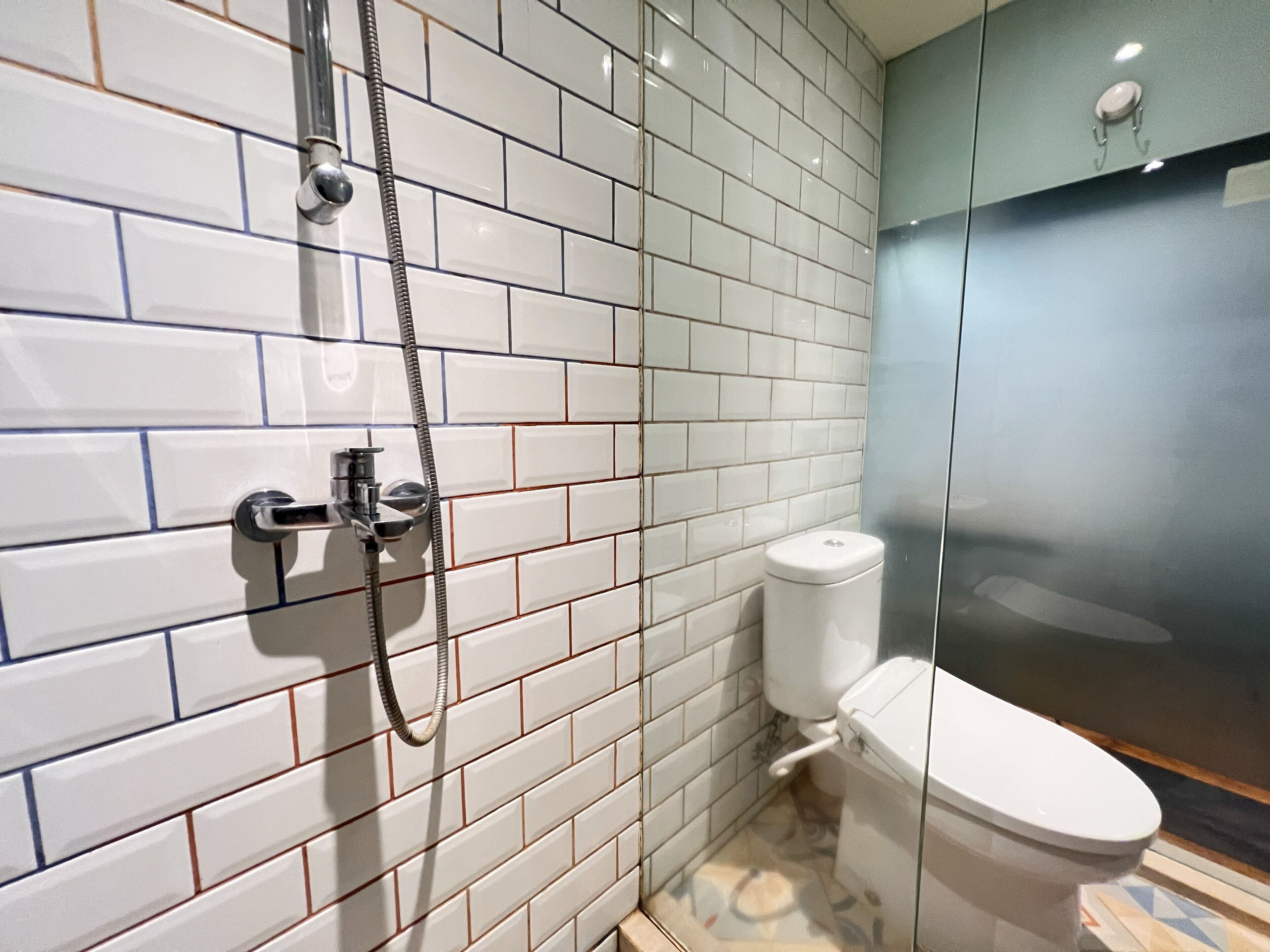A bathroom with white tiled walls, a glass shower enclosure, and a toilet.