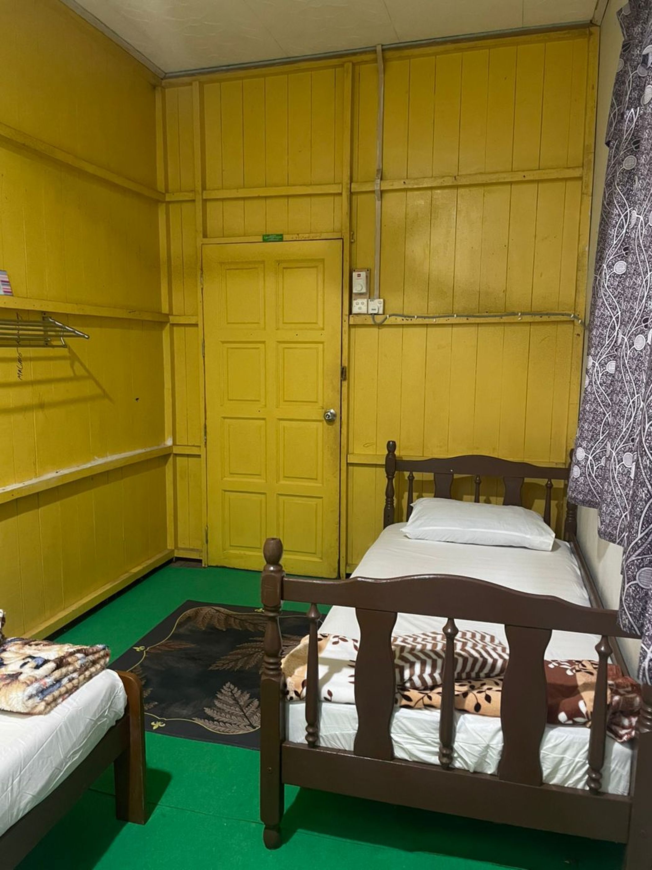 Una habitación pequeña con paredes amarillas, una cama individual, una mesita y una alfombra verde.