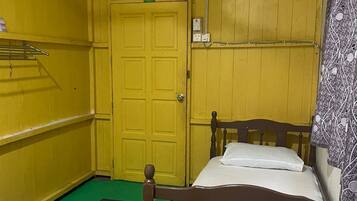 Una habitación pequeña con paredes amarillas, una cama individual, una mesita y una alfombra verde.
