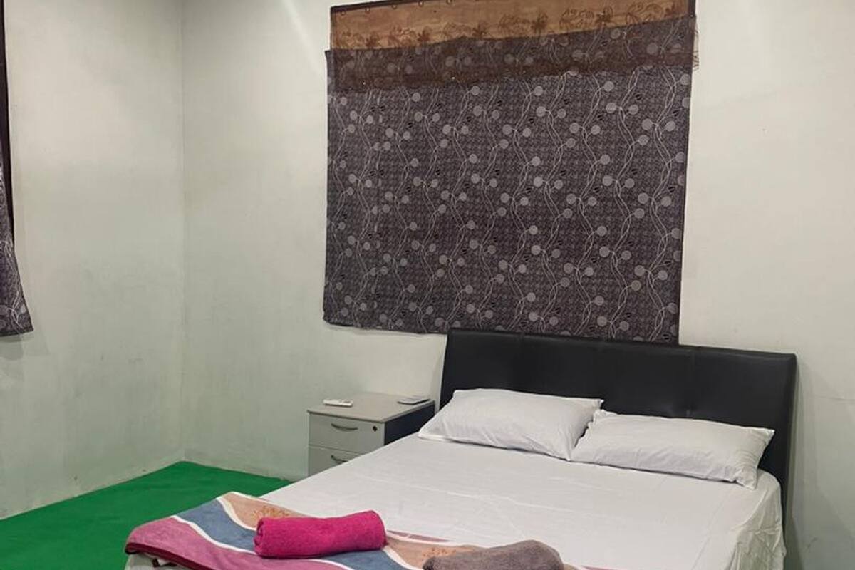A single bed with a white mattress, a black headboard, and a patterned curtain above.