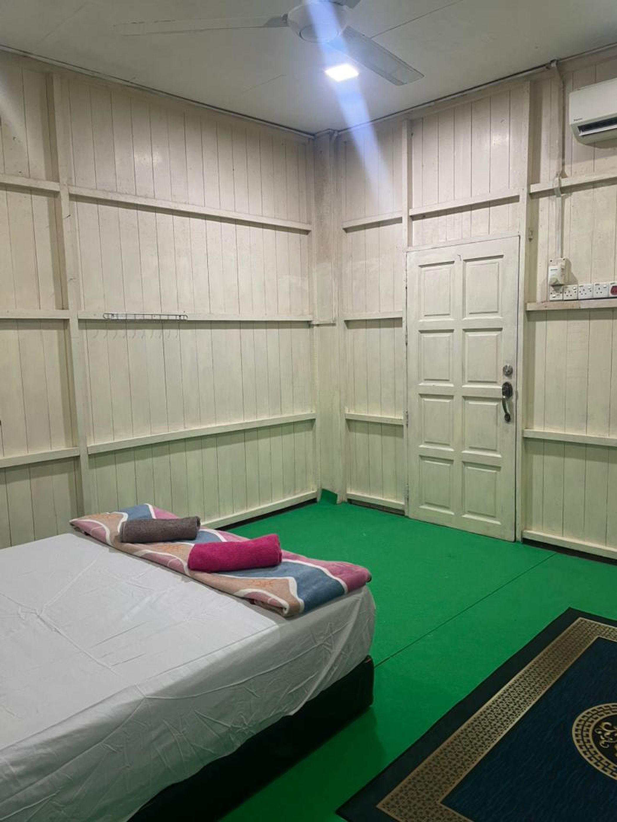 A room with a bed, green carpet, white walls, and a white door.