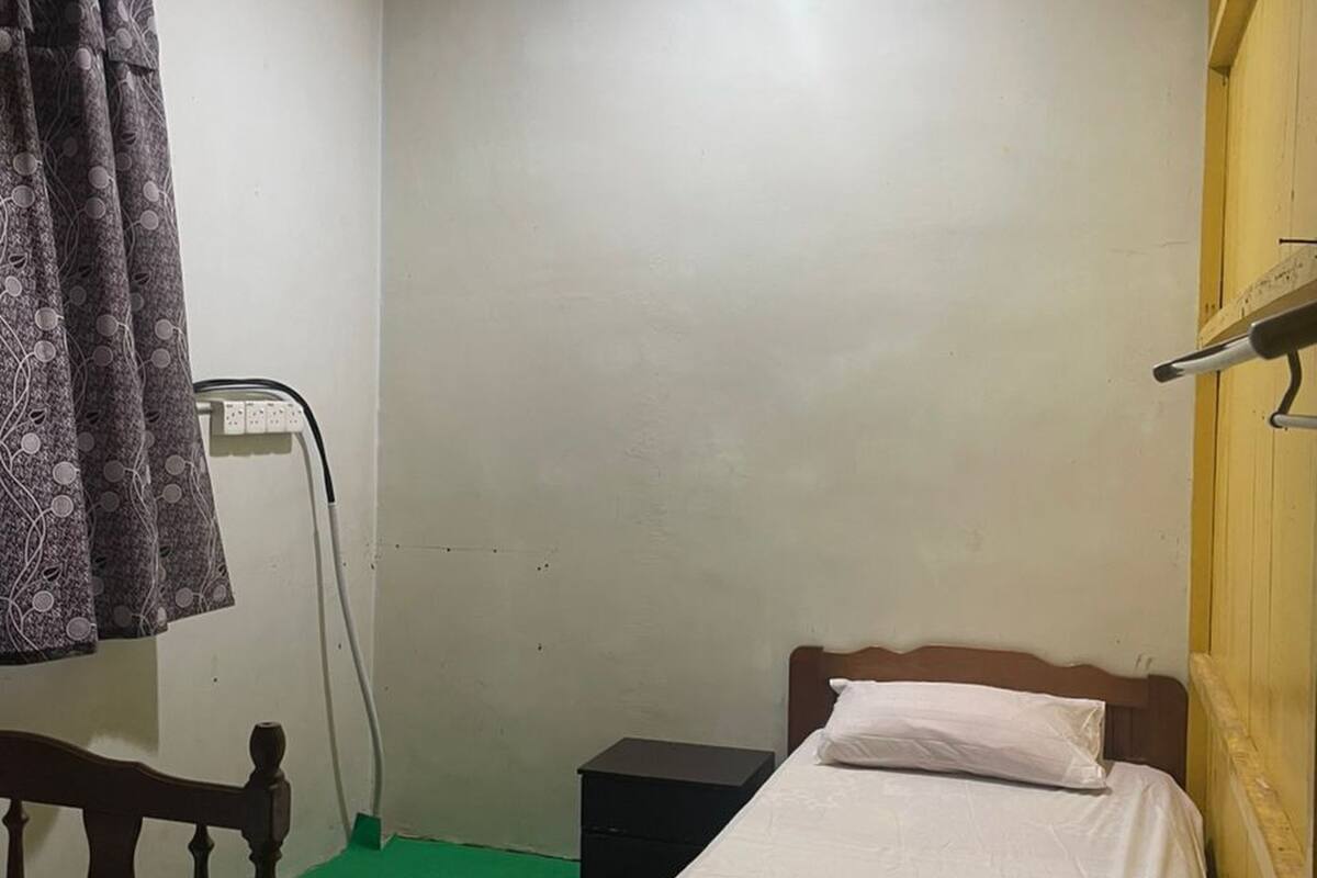 A small, simple room with two single beds, a wooden headboard, a green carpet, and a patterned rug.
