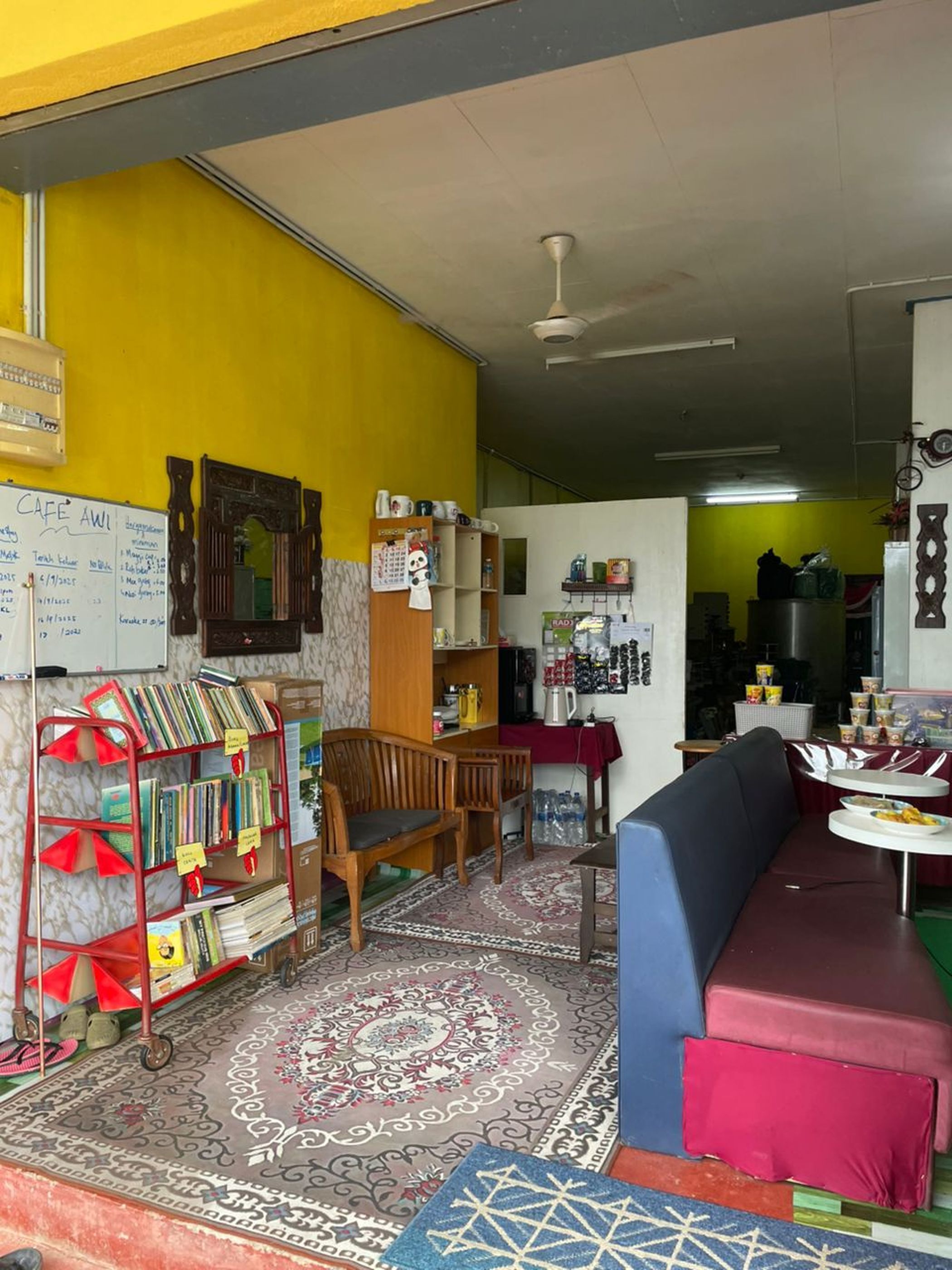 A cafe with a wooden bookshelf, a patterned rug, and a seating area with a sofa and a table.