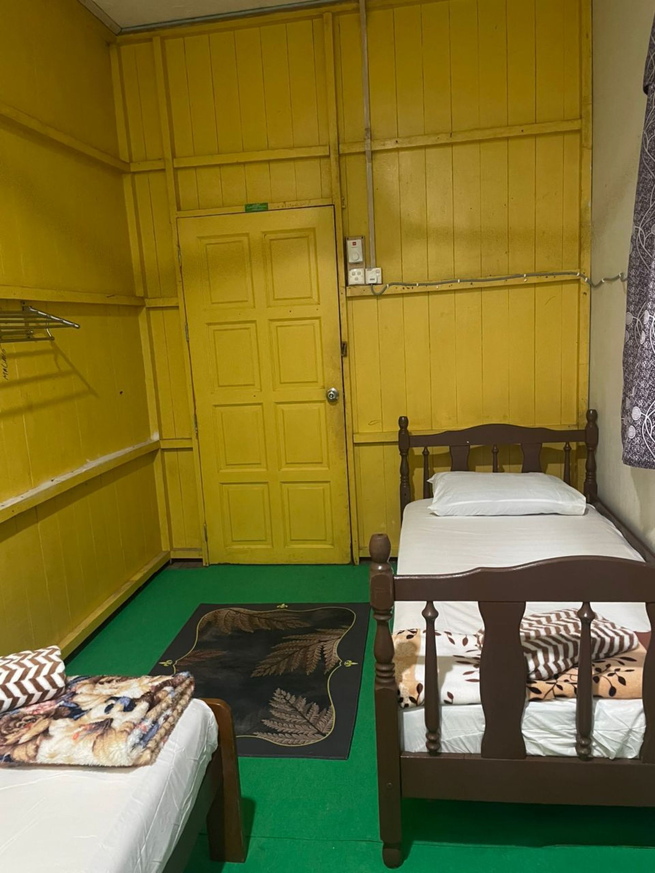 A small, yellow-walled room with two beds, a green carpet, and a door with a sign.