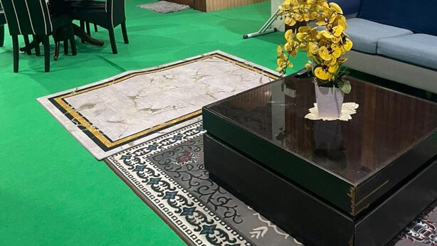 A room with a green carpet, a sofa, a dining table with chairs, a coffee table with a vase of yellow flowers, and wooden paneling on the walls. - OYO 91250 Roomstay Awie (Setiu)