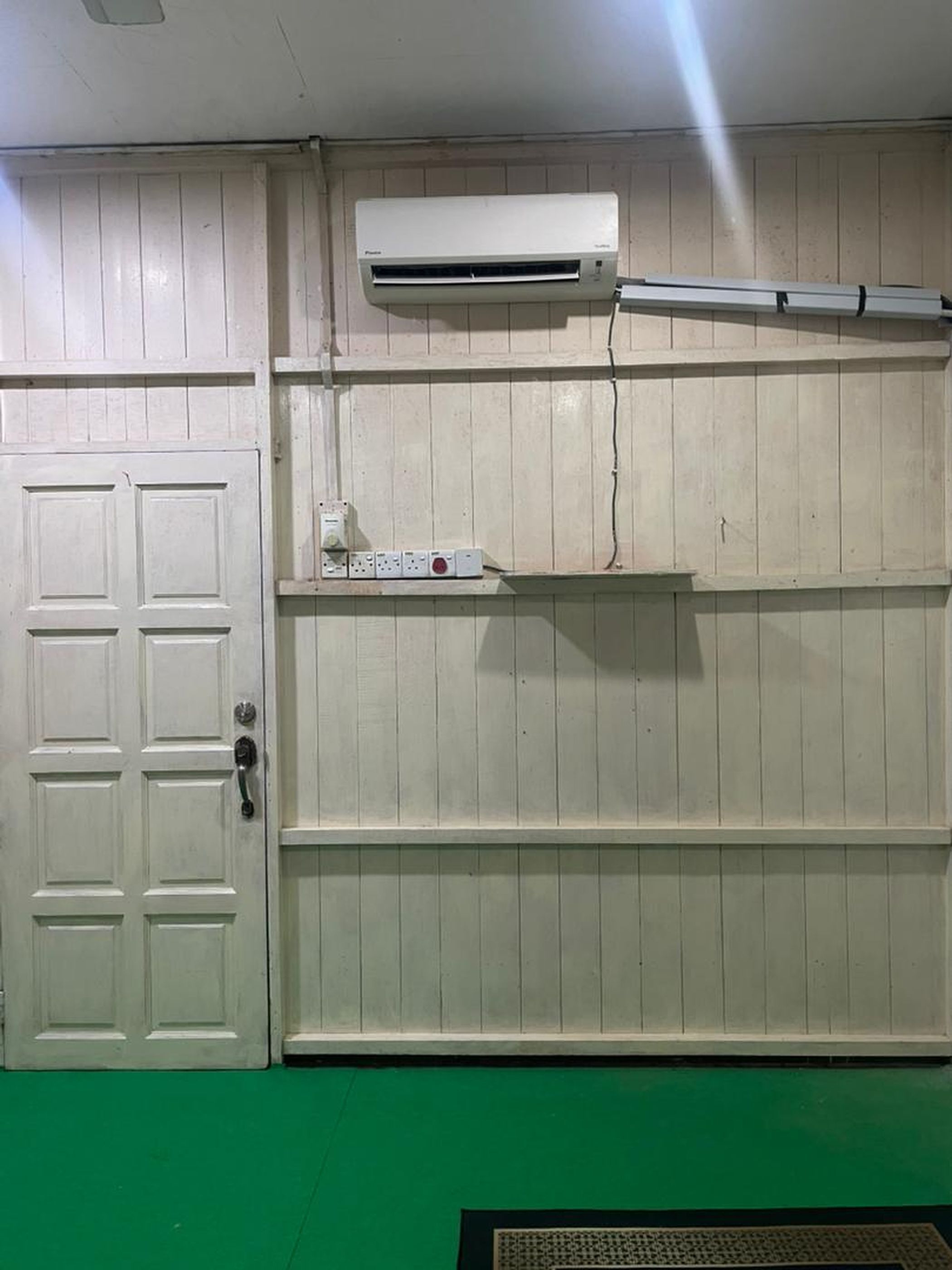 A room with a white door, a white air conditioning unit mounted on the wall, and a green floor.