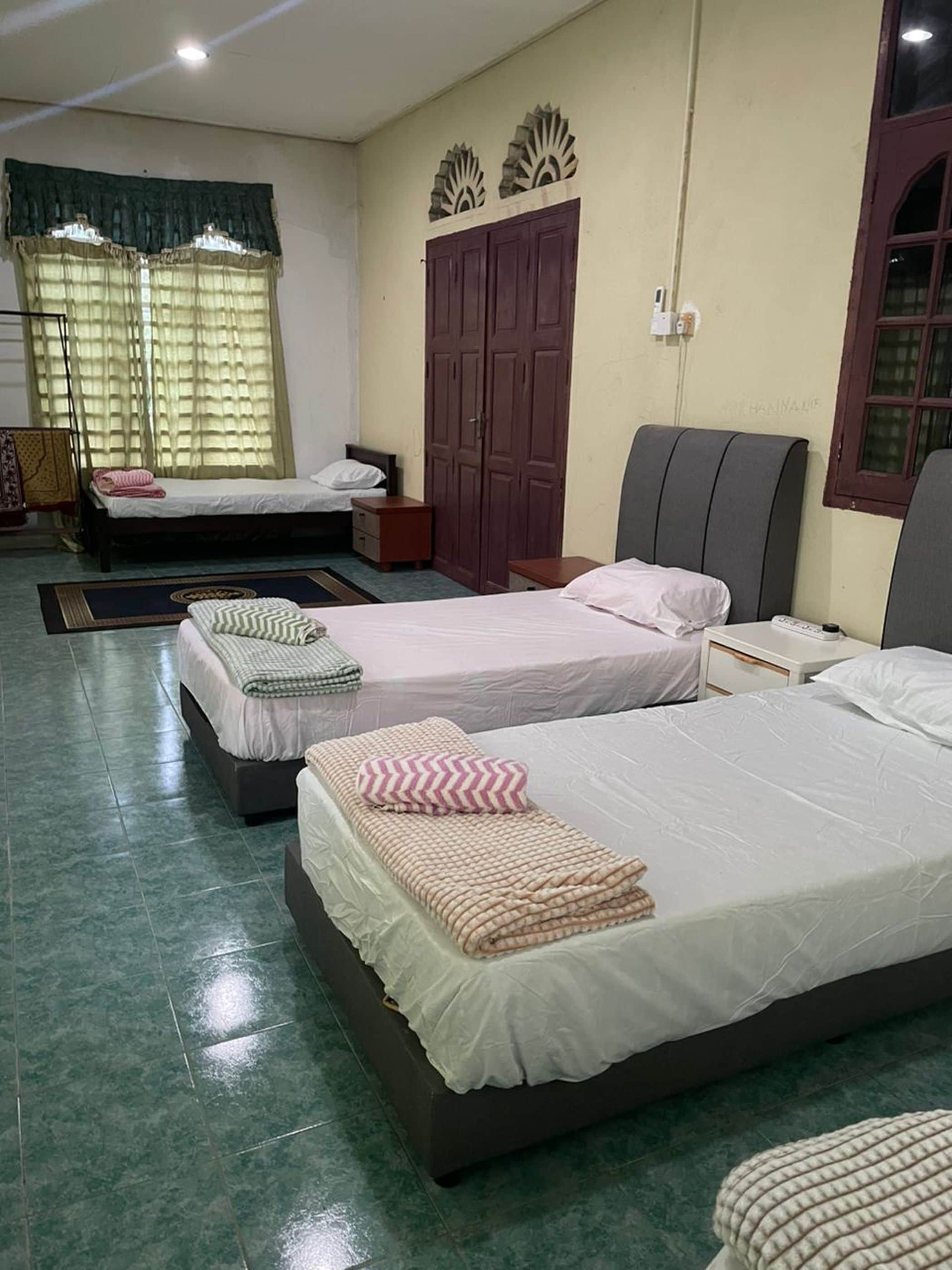 Habitación de hotel con tres camas, un armario y una ventana con cortinas.