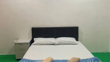 A single bed with a blue and white patterned bedspread, two rolled towels, white pillows, and a nightstand with a phone.