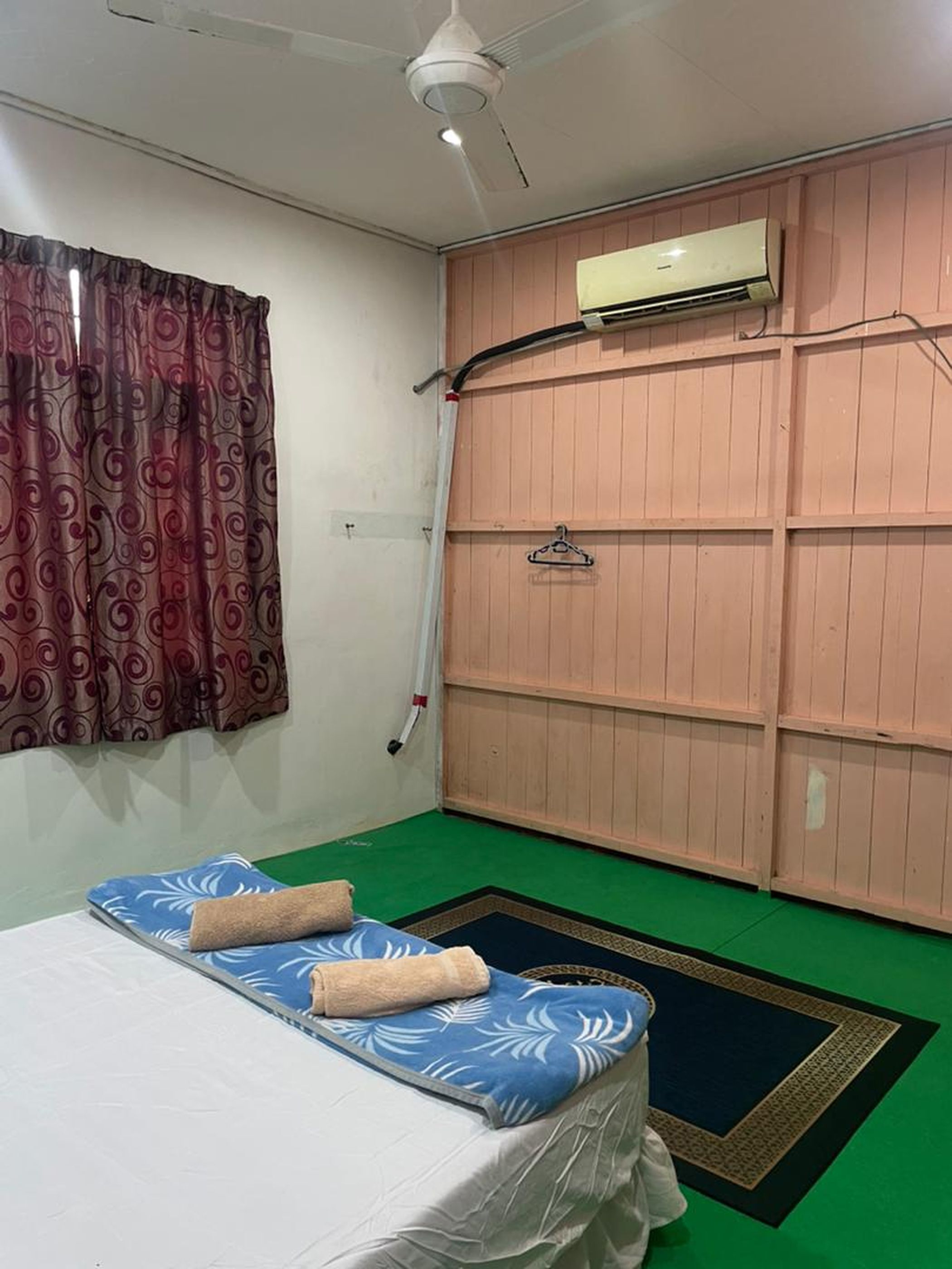 Une chambre avec un lit, un ventilateur de plafond, un climatiseur et une moquette verte.