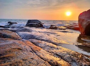Uma costa rochosa com ondas, um pôr do sol e uma grande formação rochosa.