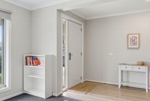 Une pièce avec une porte blanche, une bibliothèque, une petite table avec un panier, et un tableau encadré au mur.