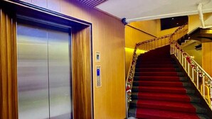 An interior hallway with a red carpet, an elevator, and a staircase with a red carpet and golden railing. - Comfy Inn Mabini Manila (Manila)