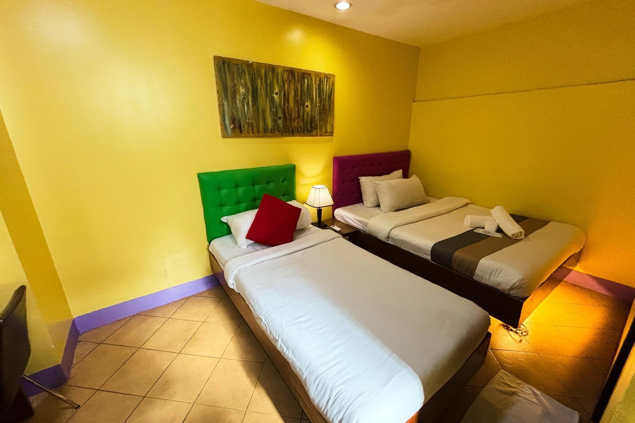 A hotel room with two beds, a green headboard, a purple headboard, and a wooden headboard.