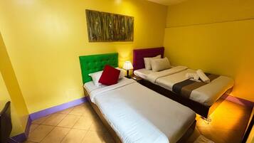 A hotel room with two beds, a green headboard, a purple headboard, and a wooden headboard.