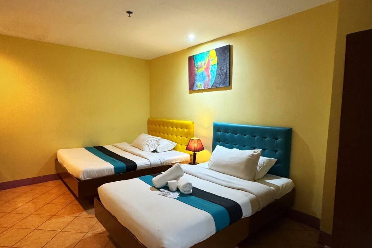 A hotel room with two beds, a colorful abstract painting on the wall, and a tiled floor.