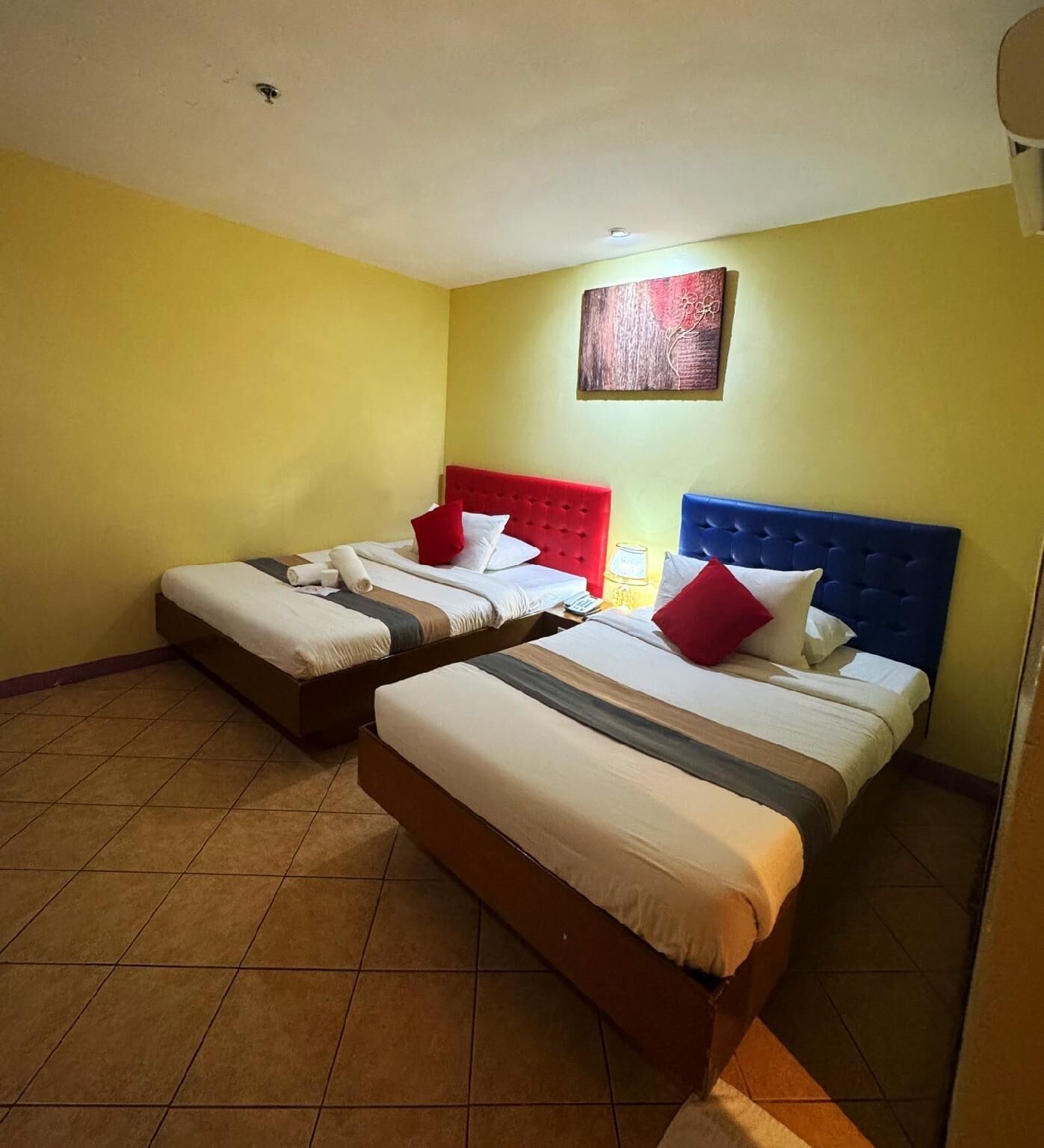A hotel room with two beds, each with a different colored headboard, and a single bed with a blue headboard.