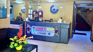 A hotel reception area with a reception desk, a sofa, a coffee table with a floral arrangement, and a staircase in the background. - Comfy Inn Mabini Manila (Manila)
