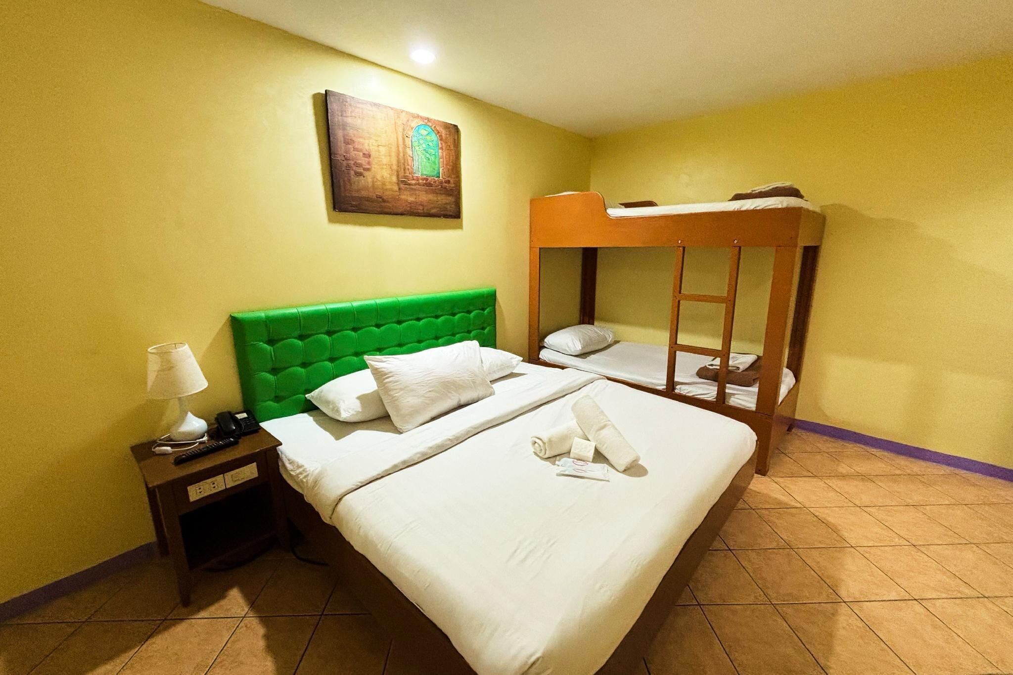 Ein Hotelzimmer mit einem Einzelbett, einem Etagenbett, einem Nachttisch mit Lampe und einem Bild an der Wand.