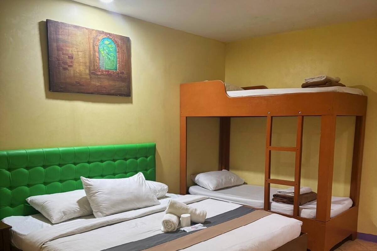 A hotel room with a large bed, a bunk bed, and a green headboard.